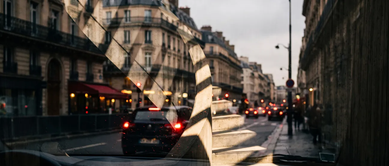 Rue parisienne vue depuis l’habitacle d’une voiture, immeubles haussmanniens et feux arrière rouges des véhicules dans la circulation